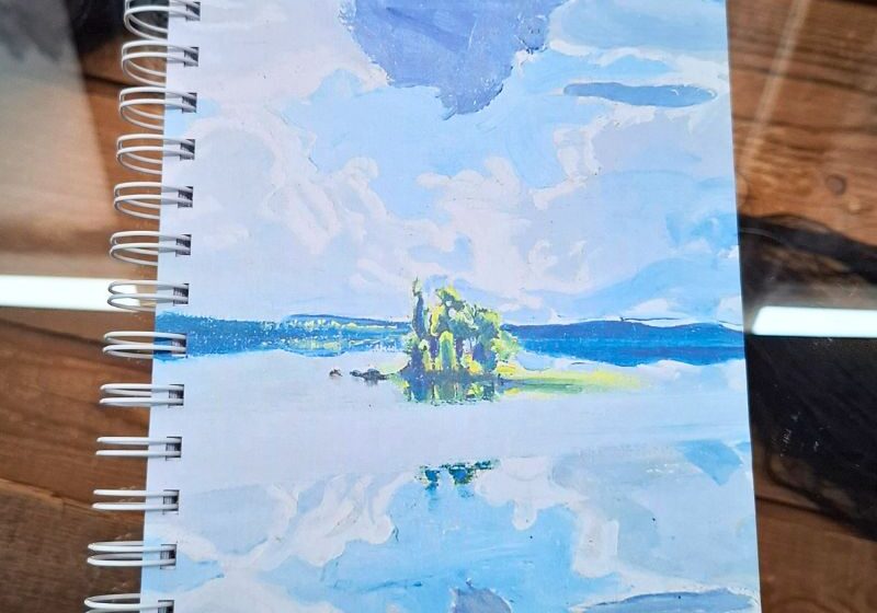 Muistikirja, jonka kannessa Pilviä järven yllä-maalaus